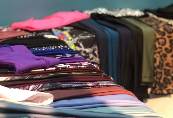 Stapel bunter, gefalteter Kleidungsstücke, darunter bedruckte und einfarbige Kleidungsstücke, werden auf einer Oberfläche ausgestellt.